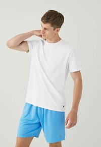 White short-sleeve T-shirt with a textured pattern, paired with blue athletic shorts. Simple round neckline and logo accent on the shirt.