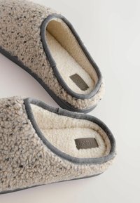 Fuzzy gray and cream slippers with a textured exterior, soft interior lining, and gray trim. Features a stitched brand label.