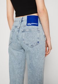 Pantalones vaqueros de denim azul claro con una cintura alta, que presentan una etiqueta brillante de Karl Lagerfeld Jeans en el bolsillo trasero y un diseño clásico de cinco bolsillos.