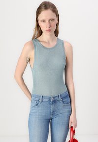 Light blue ribbed tank top with a round neckline, sleeveless design, and fitted shape. Paired with light blue jeans and a red handbag.