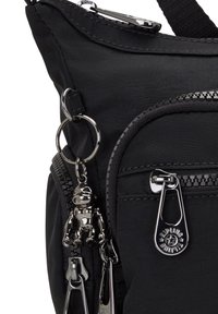 Sorth nylon skuldertaske med en lynlås lomme, hardware i sølvfarve, en nøglekæde med en abe-detalje og vinklede rembefestelser.