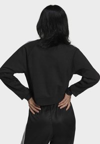 Svart kort sweatshirt med raglanärmar, slät textur, ribbad mudd och en enkel design, bärs tillsammans med matchande svarta byxor.