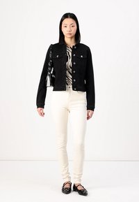 Svart denimjakke med sølvknapper, kremfargede skinny jeans og flate svarte sko med dekorative detaljer. Bølgeformet mønstrete topp under.