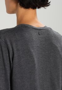 Mörkgrå stickad tröja med rund halsringning och en liten logotypetikett bak. Mjuk textur med korta ärmar och avslappnad passform.