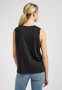 Sort ærmeløs T-shirt lavet af blødt stof, med en rund halsudskæring og en afslappet pasform, parret med lyseblå skinny jeans.