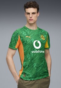 Camiseta de fútbol verde y naranja con un diseño texturizado, que presenta un logo de Vodafone en blanco y una marca Puma en negro en el pecho.