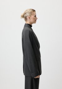 Blazer gris à rayures fines avec épaules structurées, fermeture à un seul bouton et revers crantés. Tissu lisse avec une coupe ajustée.