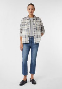 Kariertes Flanellhemd in Hellblau, Grau und Beige, kombiniert mit mittelblauen cropped Jeans und schwarzen Slippern. Glatte Textur, Knopfverschluss.