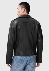 Schwarze Lederjacke mit klassischem Kragen, strukturiertem Finish und silbernen Nietenakzenten auf der Rückseite. Slim-Fit-Design mit strukturierten Schultern.