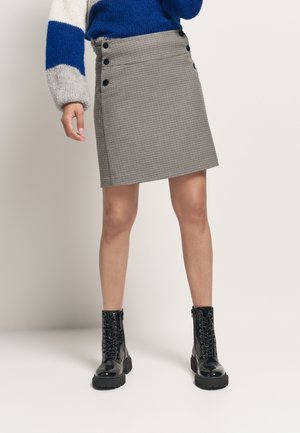 Jupe à carreaux grise avec des boutons noirs à la taille, assortie à des bottines noires à lacets. La jupe a une coupe droite et un tissu texturé.