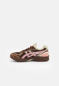 Brun och beige träningsskor med rosa och vita ränder, meshovandel och tjock sula, visad i sidoprofil på vit bakgrund.