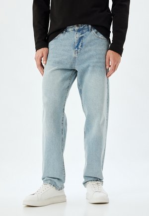 Lysblå denimjeans med en afslappet pasform, standard fem-lomme design og en falmet tekstur, parret med hvide sneakers.
