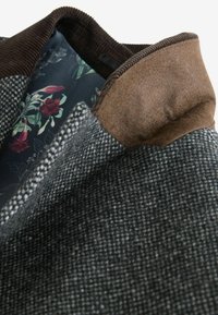 Grå ternet frakke med en brun fløjlskrave. Foret med mørkt stof med blomsterprint. Teksturen ser glat og struktureret ud.