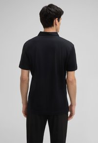 Czarny polo z krótkim rękawem o miękkiej fakturze. Posiada klasyczny kołnierz i prosty materiał, pokazany od tyłu.