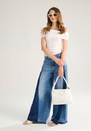 Top bianco scollato, pantaloni in denim a gamba larga in lavaggi chiari e scuri, e una borsa bianca con manici annodati. Occhiali da sole inclusi.