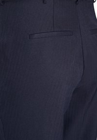 Detailný záber na tmavomodré elegantné nohavice s pohľadom na zadné vrecká a jemnú textúru látky v rybí kosti.