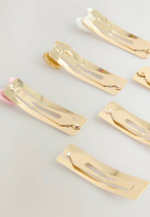 Set med hårspännen i guldmetall med en böjd form. Varje spänne har en urtagsdesign och varierande färgade ändar: rosa, vit och klar.