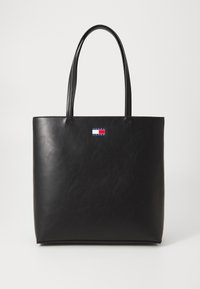 Sac fourre-tout en cuir noir avec deux longues poignées, au design minimaliste et un petit logo cousu à l'avant. Texture lisse, forme rectangulaire.