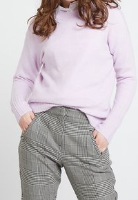Pull tricoté lavande claire avec poignets côtelés, associé à un pantalon à taille haute à carreaux noir et blanc avec poches latérales.