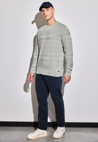 Pull long, gris clair avec des rayures horizontales, associé à un pantalon bleu marine et des baskets blanches. Le fond est blanc uni.
