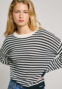 Pull en tricot rayé bleu marine et crème, avec un col rond côtelé, une coupe ample, des épaules tombantes et une texture subtile.