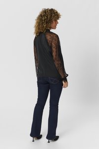 Juoda bluzonė su permatomomis nėrinių ilgomis rankovėmis ir nugara, derinama su tamsiai mėlynomis platėjančiomis džinsomis ir juodais aukštakulniais. Sklandus audinys su gėlių raštų akcentais.