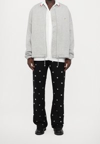 Grijze sweatvest met rits en een gestructureerd voorpand, elastische manchetten, gecombineerd met zwarte broek met zilverkleurige stippen en zwarte laarzen.