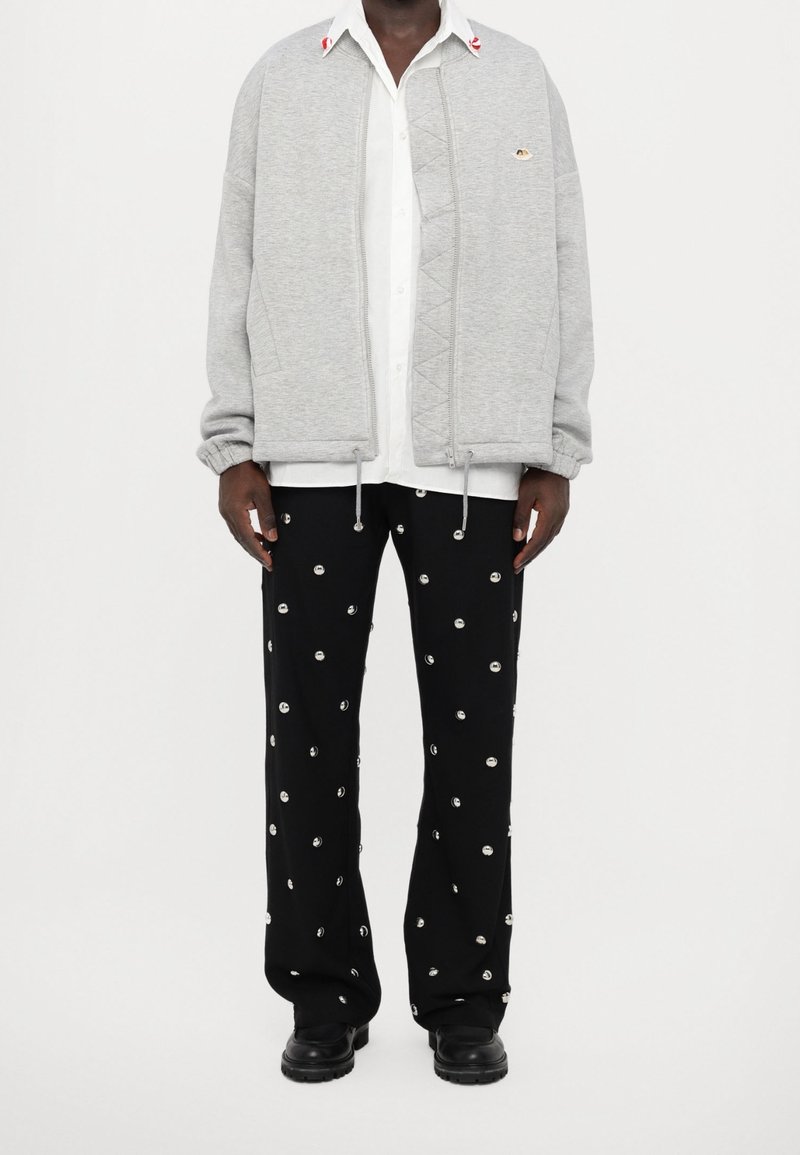 Grijze sweatvest met rits en een gestructureerd voorpand, elastische manchetten, gecombineerd met zwarte broek met zilverkleurige stippen en zwarte laarzen.