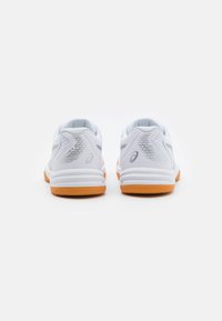 Pari valkoisia urheilukenkiä oranssilla pohjalla nähtynä takaa, brändilogo ja verkkokudostiedot valkoista taustaa vasten.