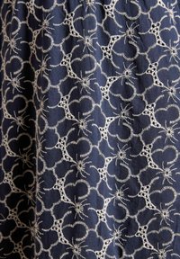 Marineblauer Stoff mit filigraner weißer Stickerei in kreisförmigen und floralen Mustern, mit erhabenen Texturen und einem weichen Finish.