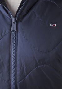 Sinih puffer jakna s gladkom teksturom, zigzag šavovima i branded zatvaračem s utisnutim "Tommy Jeans".