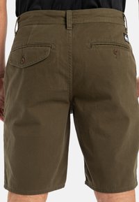 Olive green cotton shorts with a straight cut, featuring two back pockets, a button closure, and a small brand tag on the waistband.