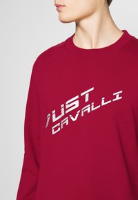 Rode sweatshirt van katoen, met een ronde hals, lange mouwen en een zilverkleurig metallic logo dat diagonaal is gedrukt.