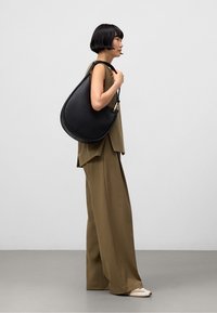 Czarna skórzana torba na ramię, w kształcie zakrzywionym, gładka w dotyku, z akcentami w złotym kolorze. Nosi do oliwkowej zielonej bluzki i spodni.