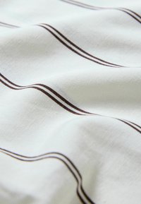 Tissu blanc avec des plis doux présentant de fines rayures parallèles brun foncé courant en diagonale sur la surface.