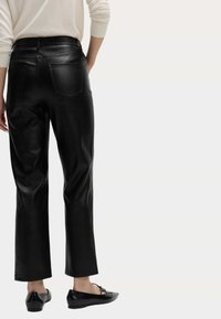 Černé kožené zkrácené kalhoty s hladkým povrchem, rovně střižené nohavice a zadními kapsami, spárované s plochými černými botami.