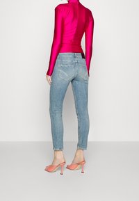 Top ajustado de color rosa brillante, de manga larga; jeans skinny de un azul claro; diseño de espalda abierta; mule rosa con tacón alto; textura de tela suave.