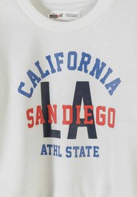 Sweat-shirt blanc avec texte bleu "CALIFORNIA", grand "LA" noir, "SAN DIEGO" en rouge et "ATHL STATE" en bleu imprimés sur le devant.