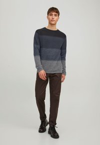 Herresweater med lange ærmer i strik med marineblå og grå vandrette striber, rund halsudskæring og struktureret stof. Kombinationen med mørkebrune bukser og støvler.