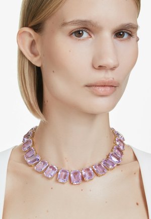 Primo piano di una donna che indossa una collana con grandi gemme rettangolari color lavanda incastonate in oro.