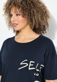 Camiseta azul marino de tela suave con un corte holgado, cuello redondo y un estampado gráfico blanco con la palabra "SELF" en el frente.