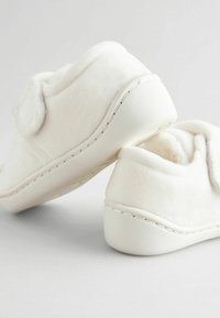 Chaussons blancs duveteux avec une texture douce, présentant un design incurvé et une semelle en caoutchouc lisse, accentués par des coutures discrètes le long du bord.