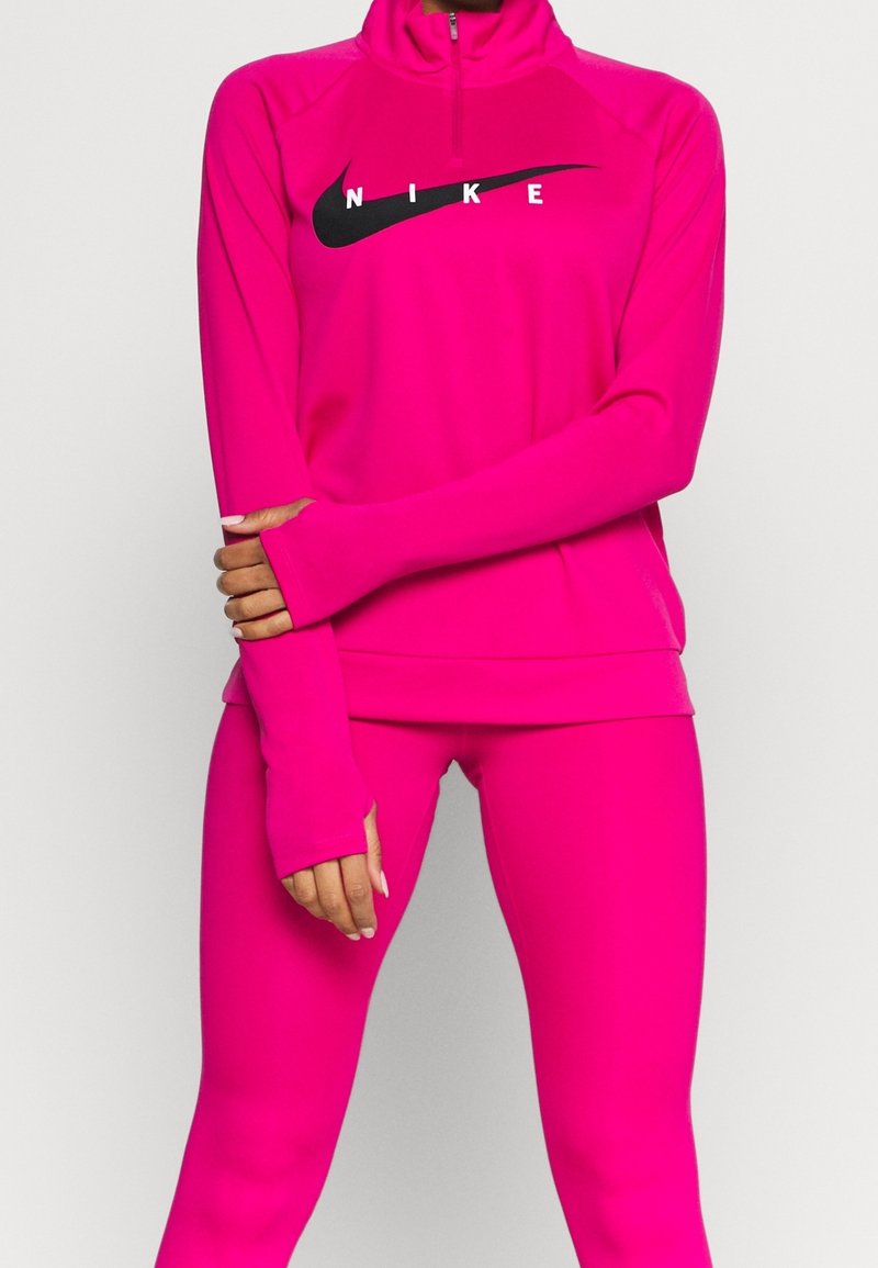 Fuchsia Zip-Hoodie und passende Leggings aus dehnbarem Material mit einem schwarzen Nike-Logo über der Brust und Daumenlöchern in den Ärmeln.