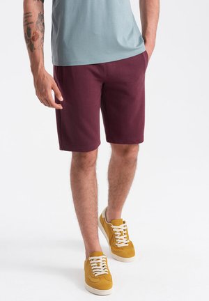 Shorts bordeaux à coupe classique, fabriqués en tissu doux ; complétés par des baskets jaunes avec des lacets blancs et un t-shirt bleu clair.