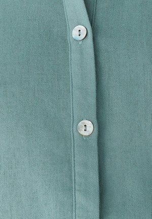 Turkizna bluza z teksturirano tkanino, z V-izrezom in dvema okroglima gumboma iz morske školjke na sprednji zadrgi.