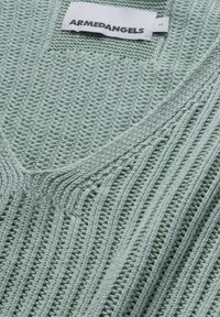 Pull vert clair en maille avec col en V, présentant un motif côtelé texturé et une étiquette cousue à l'encolure. Étiquette de taille visible.