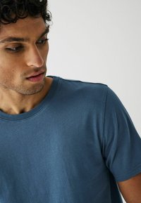 Camiseta de algodón azul de manga corta con cuello redondo, textura suave y detalle de costura visible en los hombros.