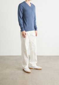 Pullover blu a scollo a V, pantaloni bianchi dal taglio morbido e sneakers bianche con dettagli beige. Il pullover ha maniche lunghe e un design aderente.