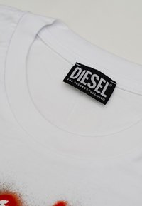 Primo piano del colletto di una maglietta bianca con un'etichetta nera del marchio Diesel che recita "PER UNA VITA DI SUCCESSO" cucita all'interno del collo.