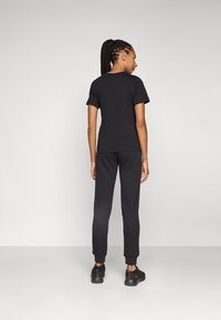 Black t-shirt and black joggers in a relaxed fit, made of soft fabric, with short sleeves and cuffs at the jogger ankles. Black sneakers worn.